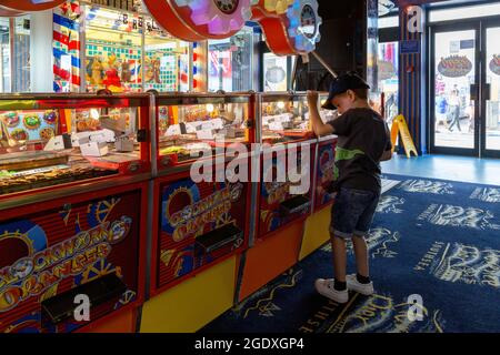 08-12-2021 Portsmouth, Hampshire, UK A Small boy playing the coin push drop arcade games in an amusements arcade Stock Photo
