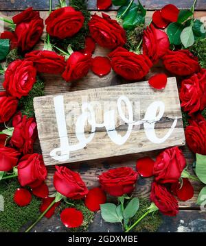 Word love handwritten on wooden board lying among red roses, copy space. Valentine's Day background. Idea of love Stock Photo