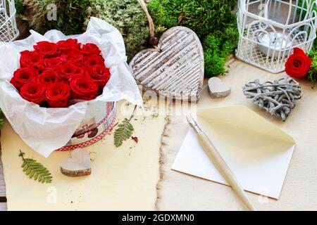 Valentine's Day decorations: box with red roses, vintage paper for greetings, wooden and wicker hearts. Stock Photo