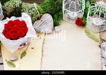 Valentine's Day decorations: box with red roses, vintage paper for greetings, wooden and wicker hearts. Stock Photo