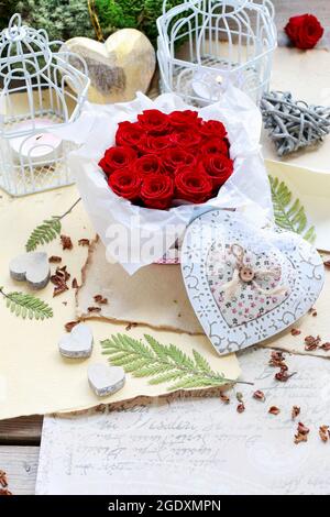 Valentine's Day decorations: box with red roses, vintage paper for greetings, wooden and wicker hearts. Stock Photo