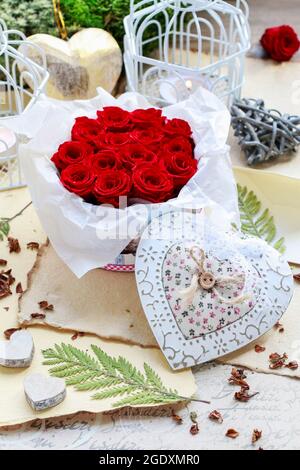 Valentine's Day decorations: box with red roses, vintage paper for greetings, wooden and wicker hearts. Stock Photo