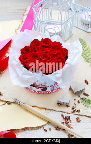 Valentine's Day decorations: box with red roses, vintage paper for greetings, wooden and wicker hearts. Stock Photo