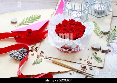 Valentine's Day decorations: box with red roses, vintage paper for greetings, wooden and wicker hearts. Stock Photo