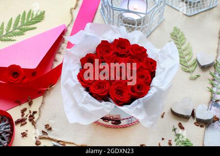 Valentine's Day decorations: box with red roses, vintage paper for greetings, wooden and wicker hearts. Stock Photo