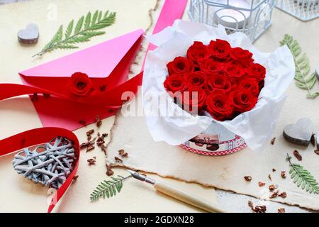 Valentine's Day decorations: box with red roses, vintage paper for greetings, wooden and wicker hearts. Stock Photo