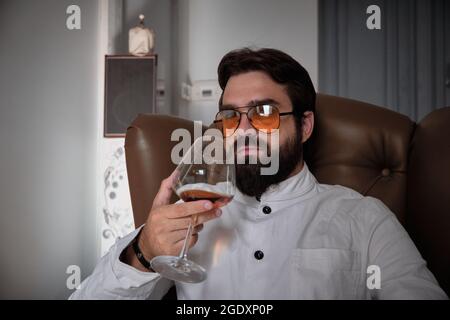 Man sits in an armchair with glass of liquor Stock Photo