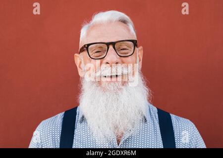 Portrait of happy hipster senior man smiling on camera with red background - Focus on face Stock Photo
