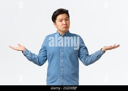 Clueless sad asian young guy dont know anything, spread hands sideways and shrugging unaware, standing clueless, cant understand, standing indecisive Stock Photo