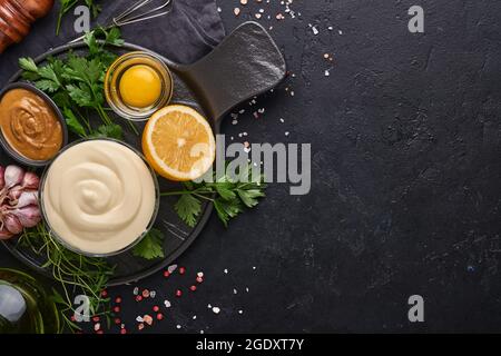 Homemade mayonnaise sauce and ingredients lemon, eggs, olive oil, spices and herbs, black background copy space. Food cooking background. Top view. Stock Photo