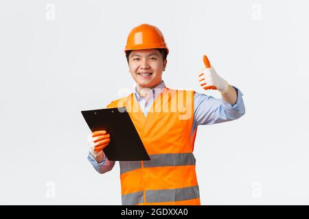 Building sector and industrial workers concept. Smiling satisfied asian chief engineer, architect making inspection showing thumbs-up in approval Stock Photo