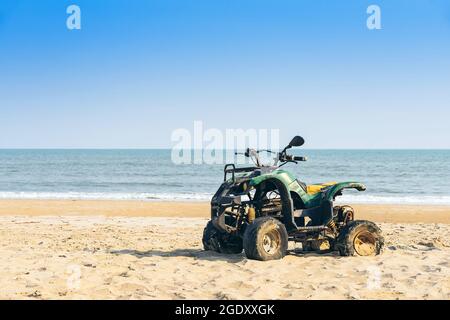 Vintage green ATV on the sandy beach. Quad ATV all terrain vehicle parked on beach, Motor bikes ready for action with summer sun flaring on bright day Stock Photo