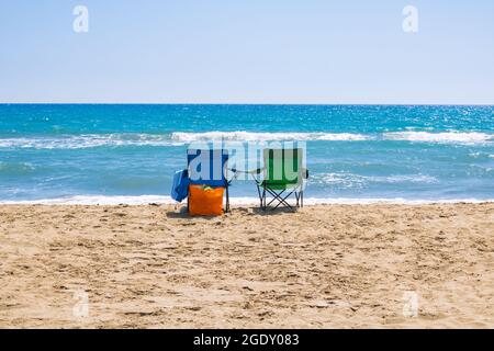 Green and blue camping chairs near the sea on the beach with an orange bag. Holiday, vacation, camping or tourism background photo. Stock Photo