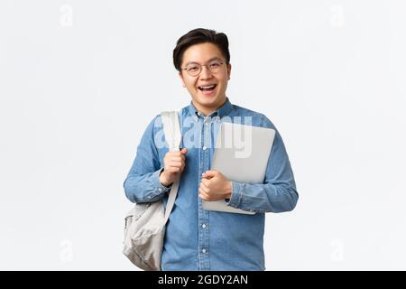 University, study abroad and lifestyle concept. Smiling cheerful asian guy in glasses standing with backpack and laptop. Student on his way to classes Stock Photo