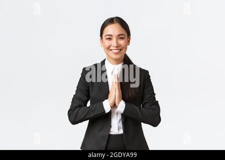 Hopeful glad asian businesswoman in black suit bowing politely and say namaste, greeting clients and smiling friendly. Thankful female manager Stock Photo