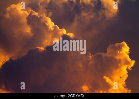 Storm clouds gather as the setting sun bathes them in a dramatic orange glow. Stock Photo