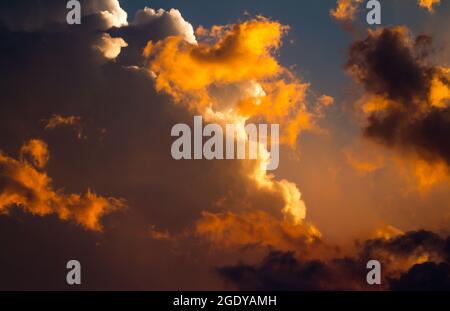 The setting sun bathes gathering storm clouds in a dramatic orange glow. Stock Photo