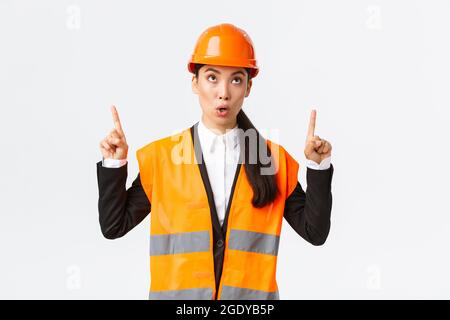 Building, construction and industrial concept. Surprised and curious asian female construction manager, engineer in safety helmet and reflective Stock Photo