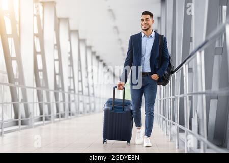 Ready For Trip. Handsome Arab Guy Walking With Suitcase At Airport Terminal Stock Photo
