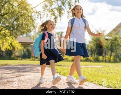Pupils of primary school. Girls with backpacks outdoors. Beginning of lessons. First day of fall. Stock Photo
