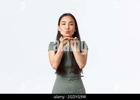 Small business owners, women entrepreneurs concept. Feminine attractive asian woman in fashionable dress, blowing mwah at camera, sending air kiss to Stock Photo