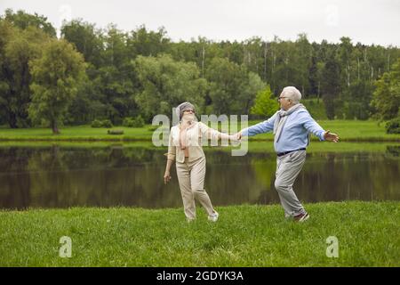 Happy senior couple taking a stroll by the river in a green park on a nice summer day Stock Photo