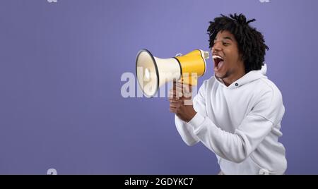 Emotional black teen guy shouting into megaphone, announcing breaking news over violet background Stock Photo