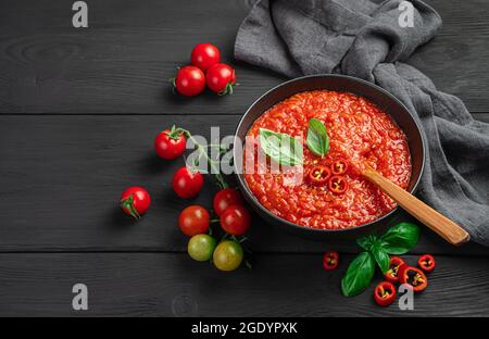 Tomato sauce in a bowl on a black background with cherry tomatoes and basil. Stock Photo