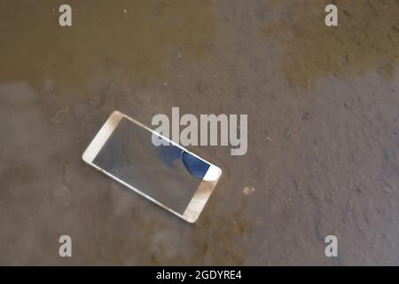 Mobile phone lying on pavement in puddle Stock Photo
