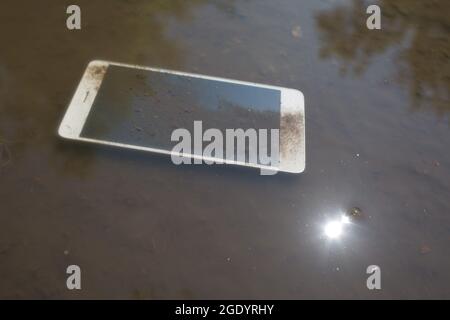 Mobile phone lying on pavement in puddle Stock Photo