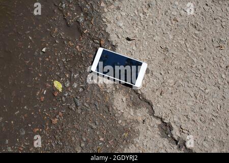 Mobile phone lying on pavement in puddle Stock Photo