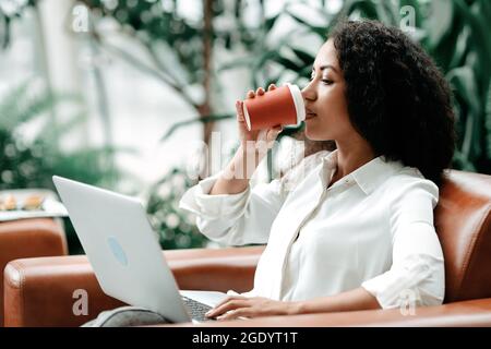 young woman drinks coffee while working on a laptop. Stock Photo