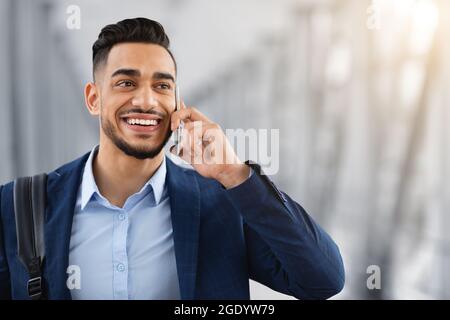 Happy Young Arab Man Talking On Cellphone At Airport Terminal, Closeup Shot Stock Photo