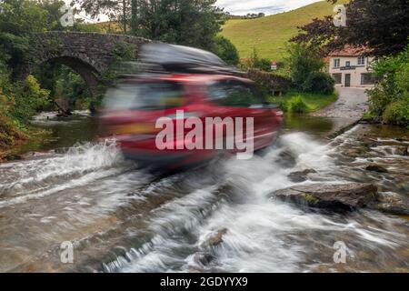 A car with a roof box drives at speed through the Badgworthy Water ford at Malmsmead in the Doone Valley, Exmoor national Park, Devon. Stock Photo