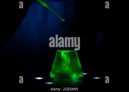 A scientist working with a green fluorescent compound in dark biochemistry laboratory for pharmaceutical development Stock Photo