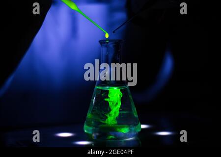 European researcher working with a green fluorescent compound in dark chemistry laboratory for pharmaceutical development Stock Photo