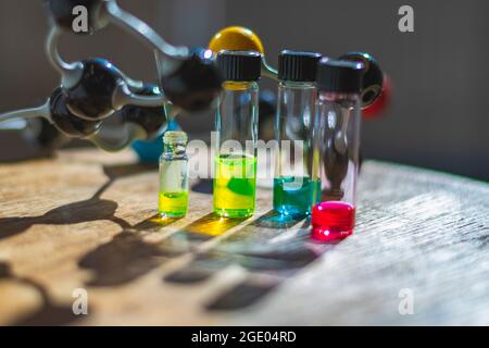 Colourful solutions in glass vials under the light with molecule model in a biochemistry laboratory for healthcare research Stock Photo