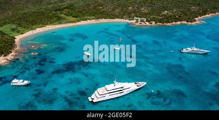 View from above, stunning aerial view of a green coastline with a white sand beach and and boats sailing on a turquoise water at sunset. Stock Photo