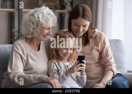 Smiling three generations of women use cellphone together Stock Photo