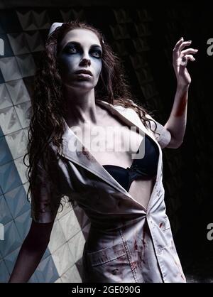 Horror shot: the weird gloomy nurse (doctor) in bloody uniform. Zombie girl (living dead) Stock Photo
