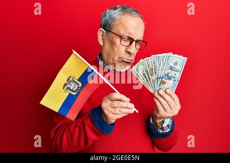 Handsome senior man with grey hair holding ecuador flag and dollars depressed and worry for distress, crying angry and afraid. sad expression. Stock Photo