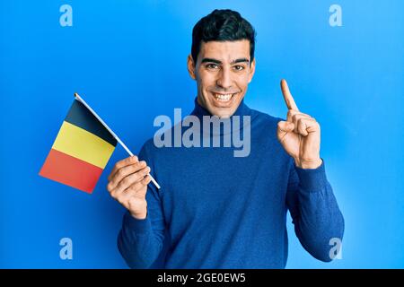 Handsome hispanic man holding belgium flag smiling with an idea or question pointing finger with happy face, number one Stock Photo
