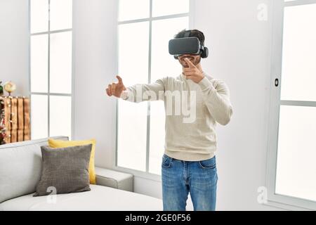 Young hispanic man smiling happy using 3d vr glasses at home. Stock Photo