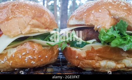 Close-up of two large DIY hamburgers in the park on a barbecue, rest and cooking on a picnic in the summer, food, delicious, bright colors. Unhealthy Stock Photo