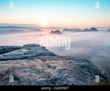 Mountain top rock, sleepy misty landscape bellow under heavy morning  fog Stock Photo