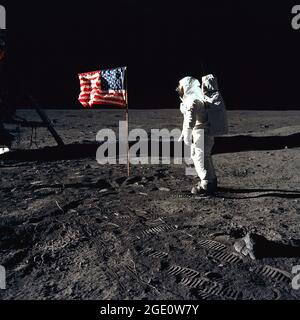 Astronaut Buzz Aldrin, lunar module pilot of the first lunar landing mission, poses for a photograph beside the deployed United States flag during an Apollo 11 Extravehicular Activity (EVA) on the lunar surface. The Lunar Module (LM) is on the left, and the footprints of the astronauts are clearly visible in the soil of the Moon. Astronaut Neil A. Armstrong, commander, took this picture with a 70mm Hasselblad lunar surface camera. While astronauts Armstrong and Aldrin descended in the LM, the 'Eagle', to explore the Sea of Tranquility region of the Moon, astronaut Michael Collins.