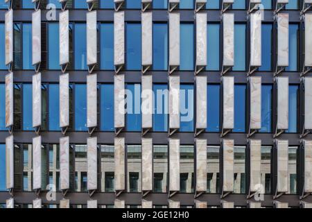 Background of exterior facade of modern building with detail of vertical stripe pattern with white panel and reflected glass windows. Stock Photo