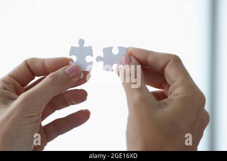 Female hands holding two white puzzle pieces closeup Stock Photo