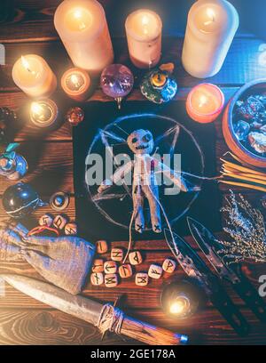 Voodoo doll studded with needles in center of magical table with candles and occult objects top view. Magic and dark spooky ritual. Retribution or revenge through witchcraft concept. Stock Photo