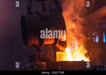 Molten metal is poured with sparks from ladle into mold. Smelting of multi-ton cast iron parts in foundry. Metallurgical plant or Steel Mill. Stock Photo